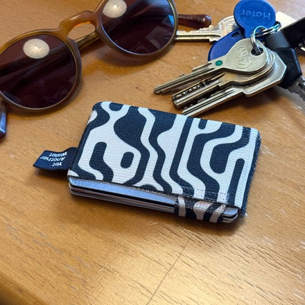 A patterned YAW wallet on a wooden table beside sunglasses and a set of keys