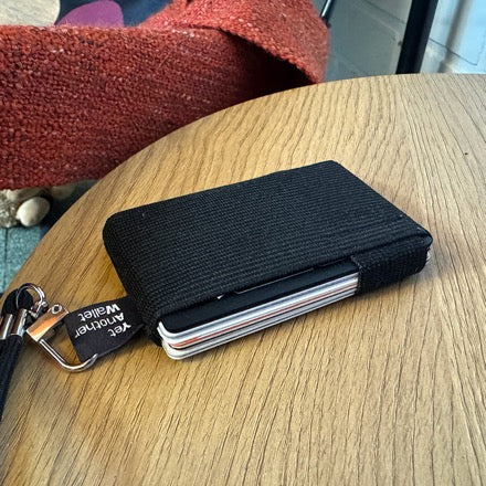 A black YAW wallet with its strap clipped on, resting on a round wooden table
