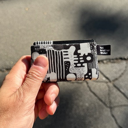 A patterned YAW wallet held up in the sun against a concrete pavement