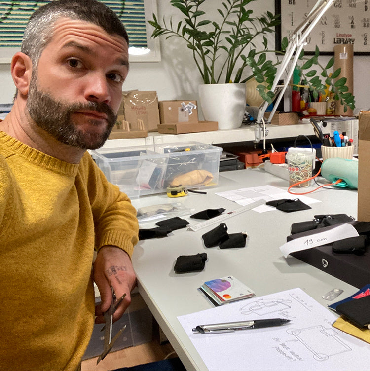 A YAW designer at a workbench covered with wallet prototypes, sketches and a tape measure